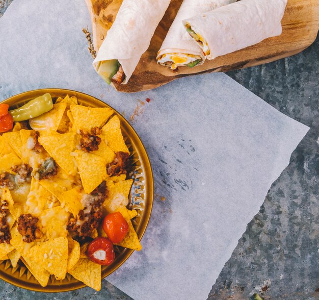 Chips de nachos mexicanos en placa con tacos mexicanos en una tabla de cortar sobre papel