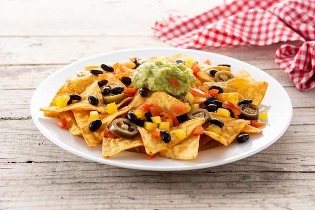 Foto gratuita chips de tortilla de nachos mexicanos con frijoles negros, guacamole, tomate y jalapeño sobre mesa de madera