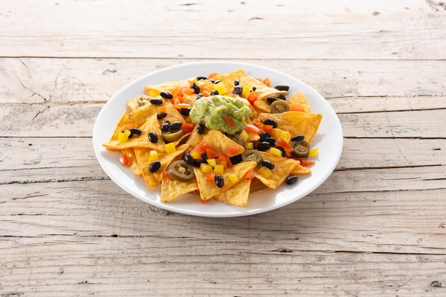 Chips de tortilla de nachos mexicanos con frijoles negros, guacamole, tomate y jalapeño sobre mesa de madera