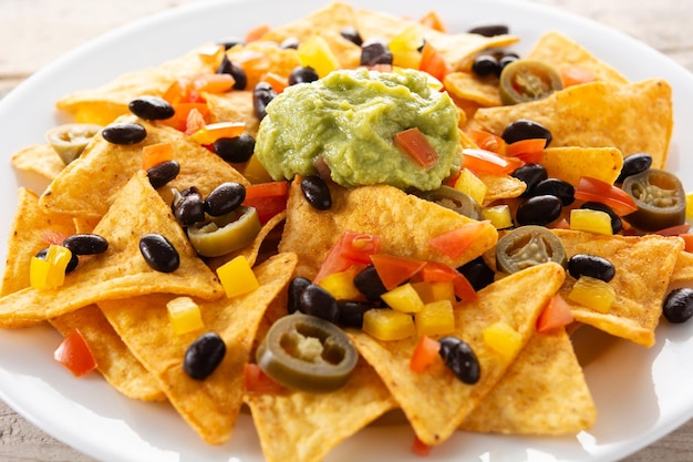 Chips de tortilla de nachos mexicanos con frijoles negros, guacamole, tomate y jalapeño sobre mesa de madera