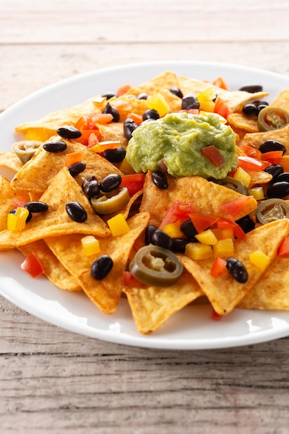 Chips de tortilla de nachos mexicanos con frijoles negros, guacamole, tomate y jalapeño sobre mesa de madera