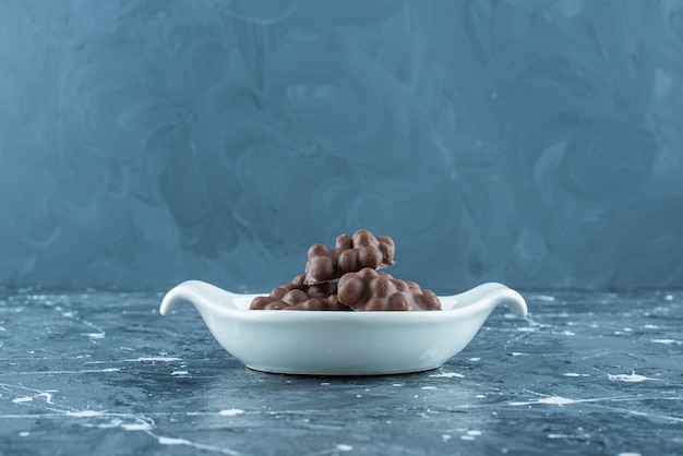 Foto gratuita chocolate con avellanas en un bol, sobre la mesa azul.