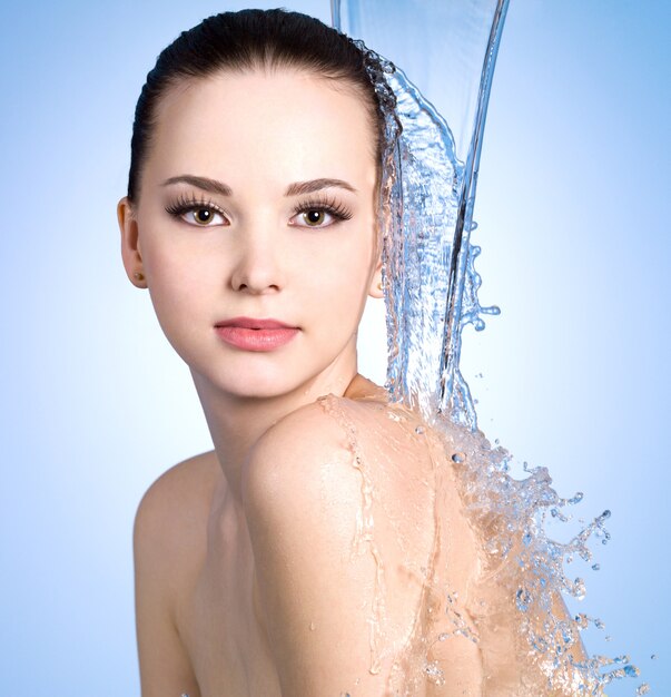 Chorro de agua cayendo sobre la mujer joven con piel hermosa - pared azul