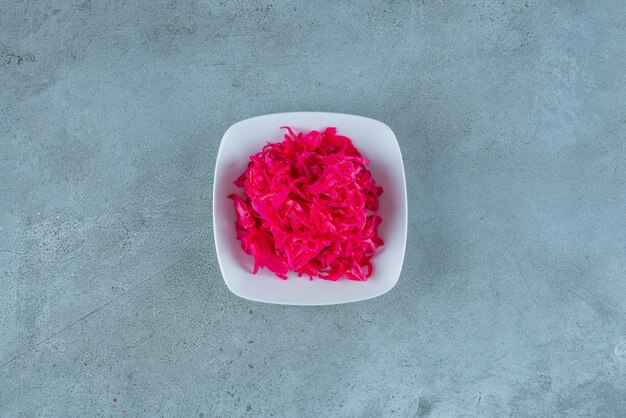 Chucrut fermentado rojo picado sabroso en un cuenco, sobre la mesa azul.