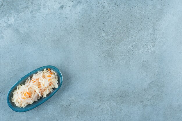 Chucrut fermentado con zanahorias en una placa de madera, sobre la mesa azul.