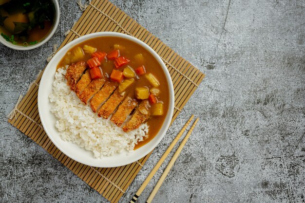 Chuleta de cerdo frita al curry con arroz sobre superficie oscura