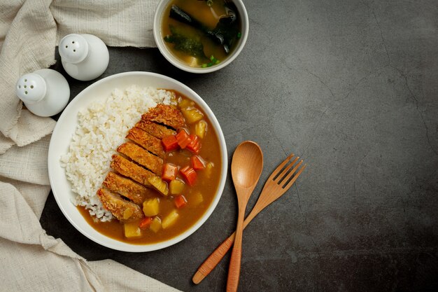 Chuleta de cerdo frita al curry con arroz sobre superficie oscura