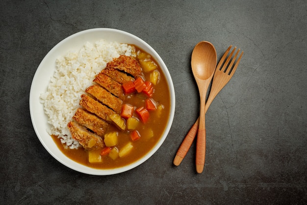 Chuleta de cerdo frita al curry con arroz sobre superficie oscura