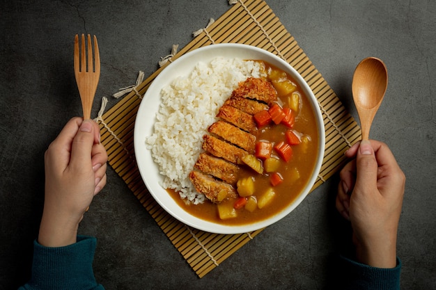 Chuleta de cerdo frita al curry con arroz sobre superficie oscura