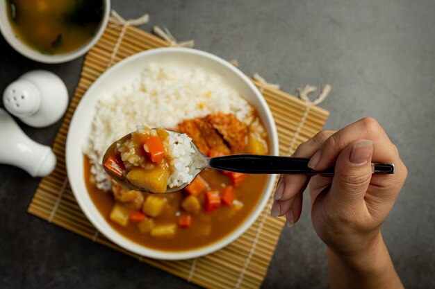 Chuleta de cerdo frita al curry con arroz sobre superficie oscura