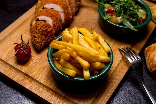 Chuleta estilo Kiev en la tabla de madera con papas fritas rúcula tomate pepino salsa vista lateral