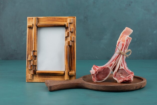 Chuletas de cordero crudo sobre tabla de madera con marco de imagen.