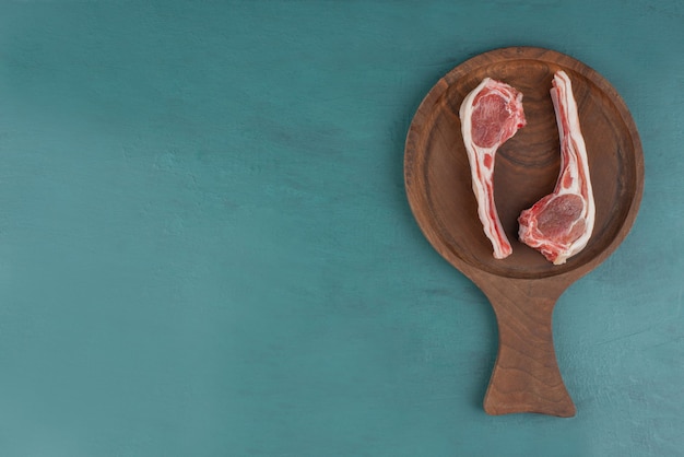 Chuletas de cordero crudo sobre tabla de madera.