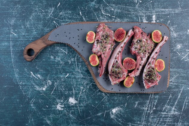 Chuletas de costilla crudas en tabla de madera con higos y hierbas secas.