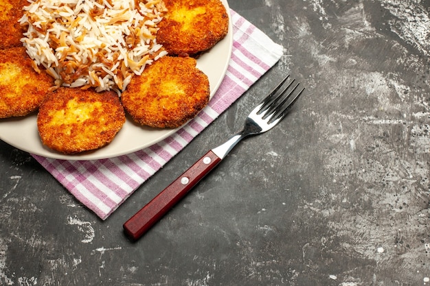 Chuletas fritas de media vista superior con arroz cocido en un plato de carne de superficie oscura