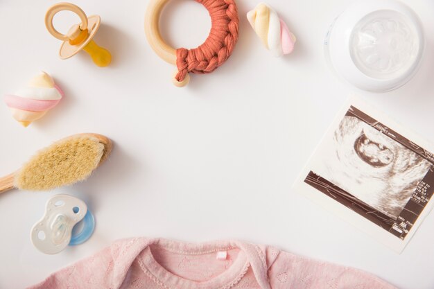 Chupete; malvavisco; cepillo; juguete; botella de leche; Foto de sonografía y baby onesie sobre fondo blanco