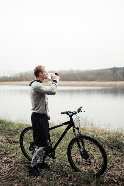 Foto gratuita ciclista, agua potable, de, botella, posición, cerca, el, lago