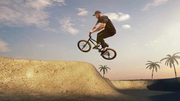 El ciclista de BMX está realizando trucos en el skatepark al atardecer