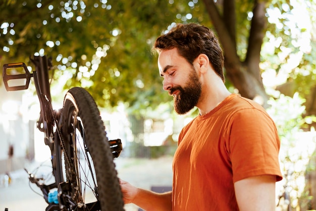 Foto gratuita un ciclista masculino activo y decidido reparando con confianza el borde de la bicicleta e inspeccionando los neumáticos para el ciclismo de ocio al aire libre. un hombre dedicado y amante de los deportes que realiza el mantenimiento de la bicicleta es una herramienta de trabajo esencial.