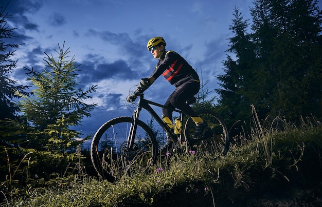 Ciclista masculino alegre montando en bicicleta por la noche