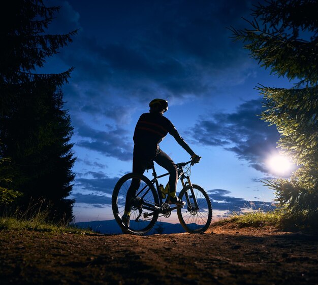 Ciclista masculino sentado en bicicleta bajo un hermoso cielo nocturno