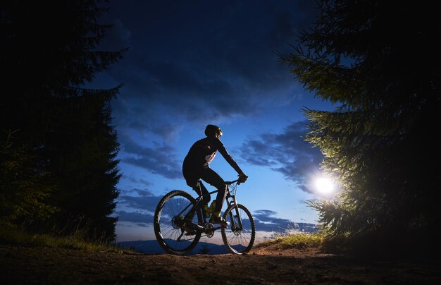 Ciclista masculino sentado en bicicleta bajo un hermoso cielo nocturno