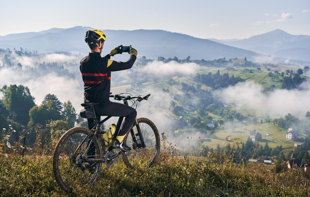 Ciclista masculino tomando fotos de montaña con teléfono inteligente