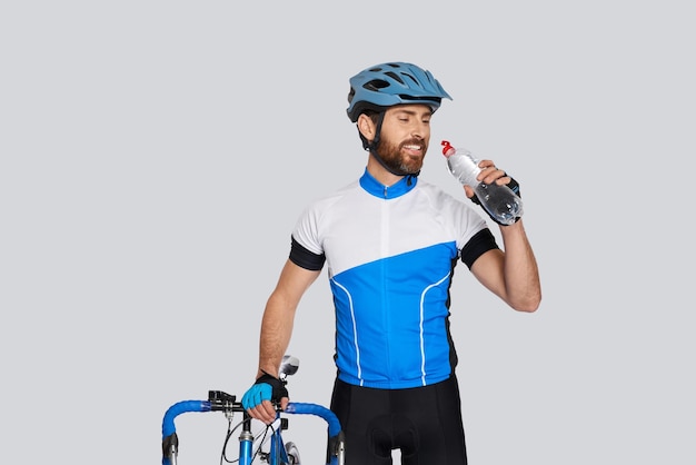 Foto gratuita ciclista musculoso con casco bebiendo agua mientras descansa en el retrato de estudio de un atleta barbudo