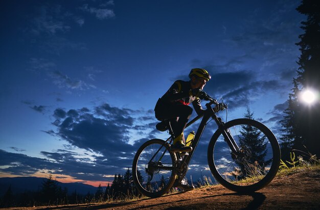 Ciclista sentado en bicicleta bajo el cielo nocturno nublado