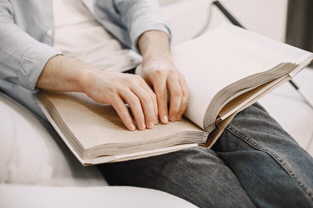 Ciego leyendo un libro en braille en el sofá. Personas discapacitadas