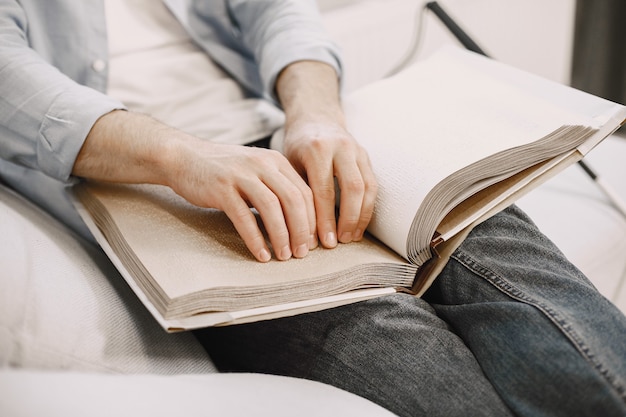 Ciego leyendo un libro en braille en el sofá. Personas discapacitadas