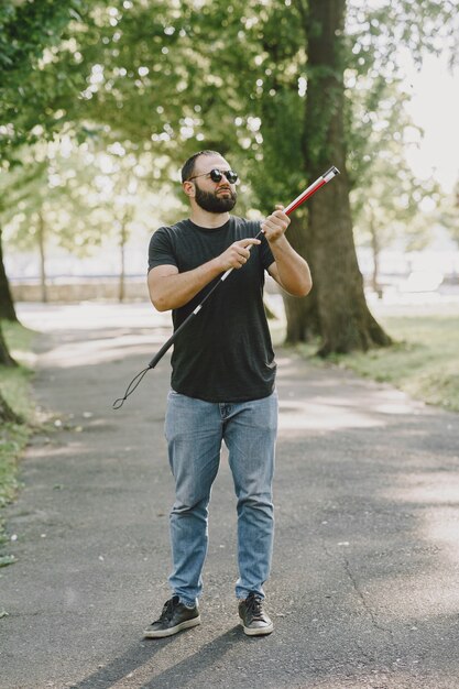 Ciego. Personas con discapacidad, minusválido y vida cotidiana. Hombre con discapacidad visual con bastón, pasos descendentes en el parque de la ciudad.