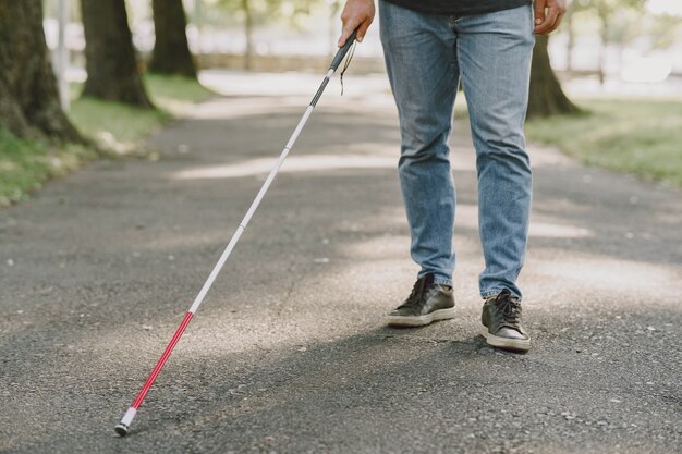 Ciego. Personas con discapacidad, minusválido y vida cotidiana. Hombre con discapacidad visual con bastón, pasos descendentes en el parque de la ciudad.