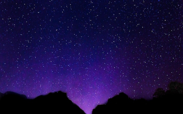 Cielo nocturno con muchas estrellas brillantes con fondo borroso de montaña.