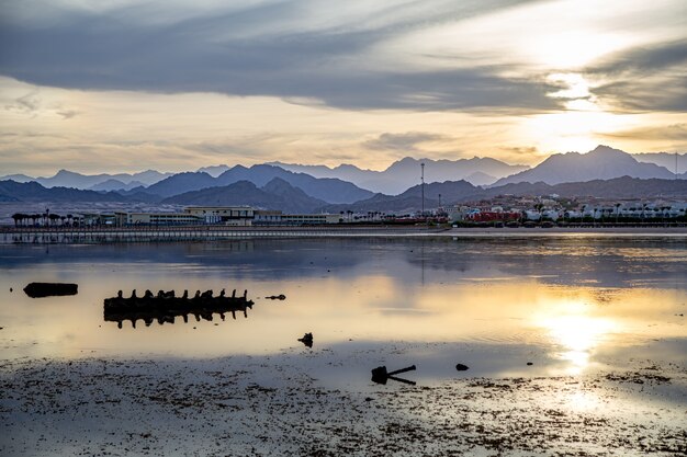 El cielo del paisaje se refleja en el mar a la luz del escenario. Costa de la ciudad con montañas en el horizonte.