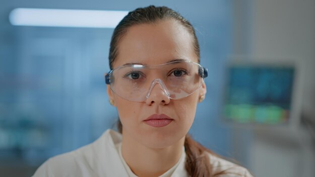 Científica con gafas protectoras en laboratorio, mirando a cámara. Retrato de investigador de bioquímica con gafas de laboratorio para la seguridad en el trabajo de desarrollo químico. De cerca