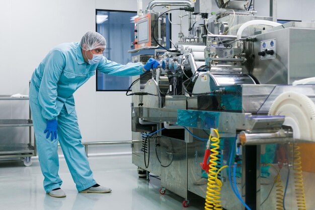 Científico caucásico doblado en traje de laboratorio azul tratando de arreglar la máquina de fabricación con ejes