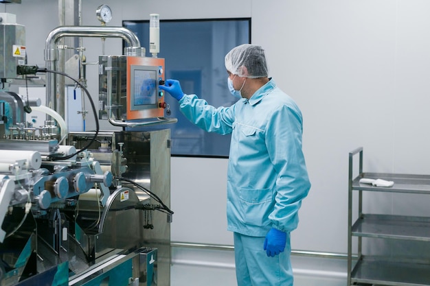Científico caucásico con traje de laboratorio azul configura el panel de control en una gran sala limpia