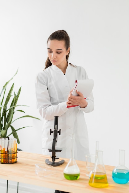 Científico femenino con bata de laboratorio mirando al microscopio