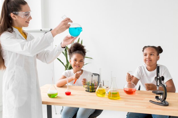 Científico femenino enseñando química a las chicas mientras sostiene una poción