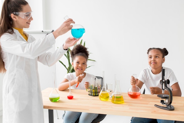 Científico femenino enseñando química a las chicas mientras sostiene una poción
