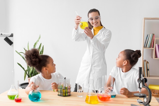 Científico femenino enseñando química a las niñas mientras sostiene el tubo