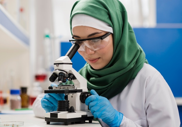 Científico femenino con hijab y microscopio en el laboratorio