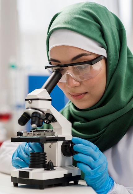Científico femenino con hijab y microscopio en el laboratorio