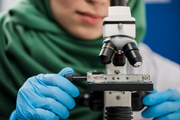 Científico femenino con hijab trabajando en laboratorio con microscopio