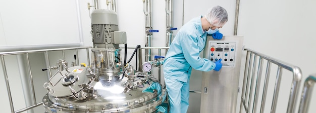 Científico de imagen panorámica con traje de laboratorio azul, panel de control cerca de grandes tanques cromados