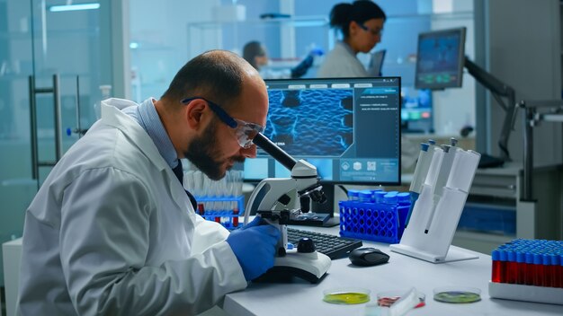 Científico de investigación médica que realiza el desarrollo de vacunas bajo microscopio digital en un laboratorio de ciencias biológicas aplicadas