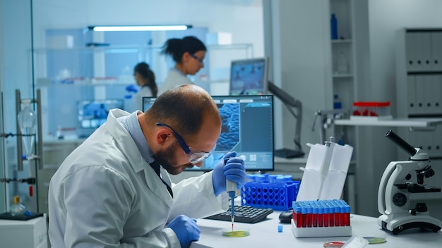 Científico en el laboratorio médico que examina el descubrimiento de fármacos poniendo una muestra de sangre en una placa de Petri con una micropipeta