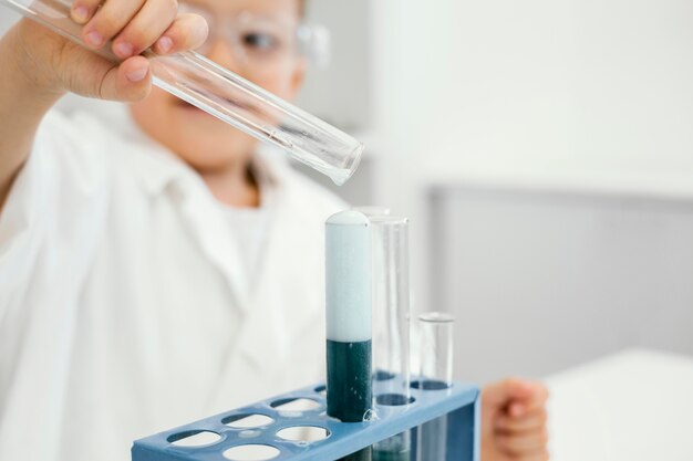 Científico de niño sonriente en el laboratorio con tubos de ensayo experimentando