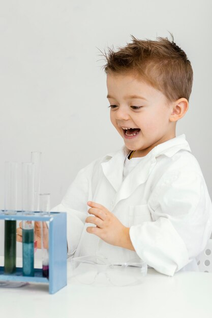 Científico de niño sonriente en el laboratorio con tubos de ensayo